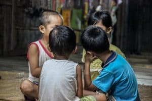 Four young children sitting on the floor in a tight circle facing one another.