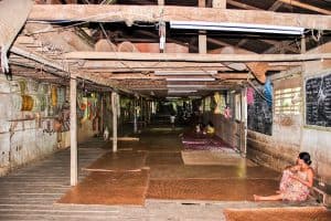 A woman sits on the floors against a wall in a long corridor room - a tribal Iban Longhouse in Borneo