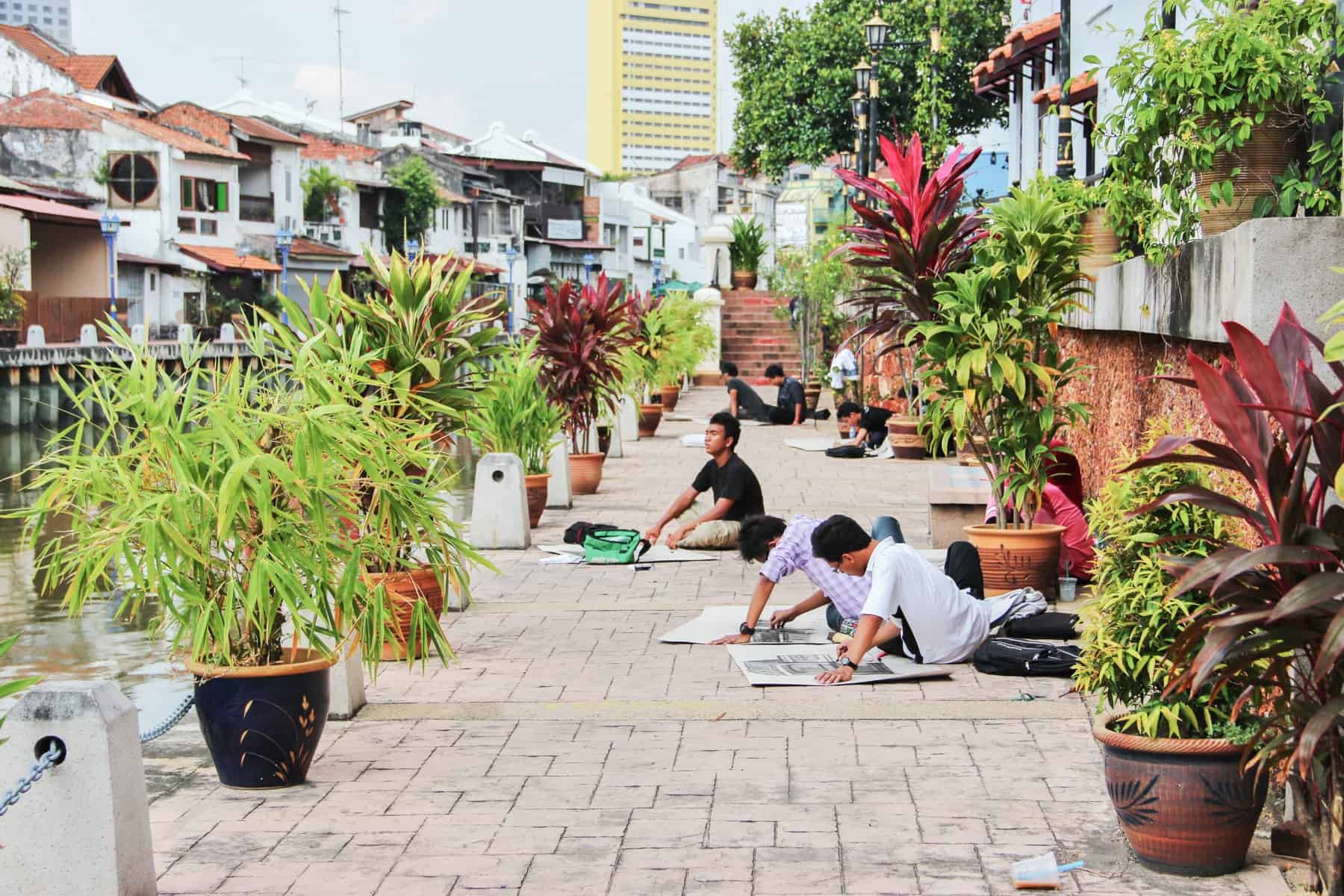 Locals in Melaka sitting on the pavement that lines the river as part of a collective sketching club 