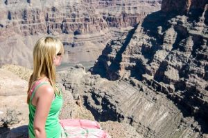 A woman sits on a rcky surface overlooking the grand canyon on a day trip from Las Vegas.