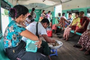 Local people holding baskets and selling food on the mint green painted and wooden interior train, known as the Yangon Circular Train in Myanmar