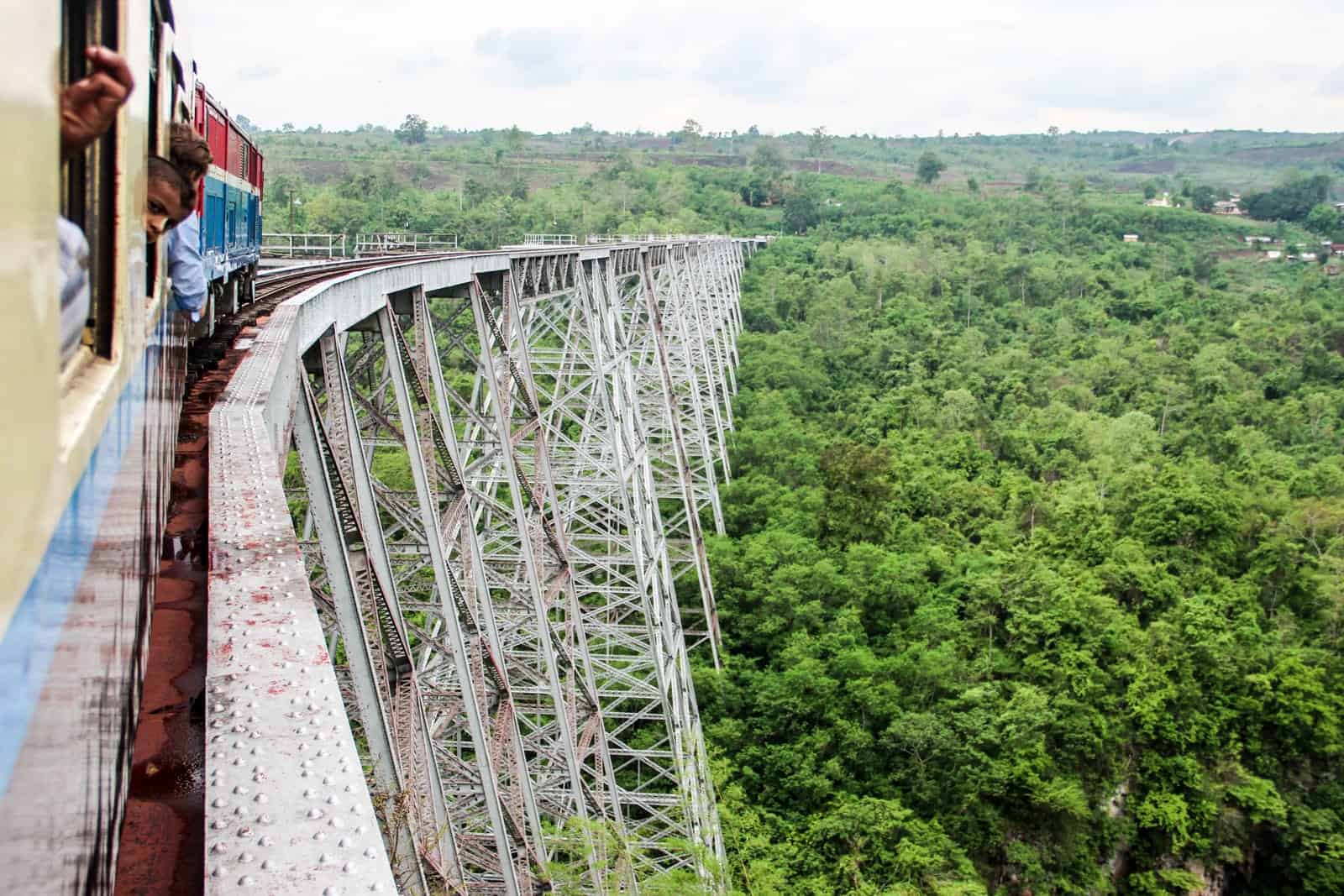 A train crossing the highest railway bridge in Myanmar, above thick jungle forest. 