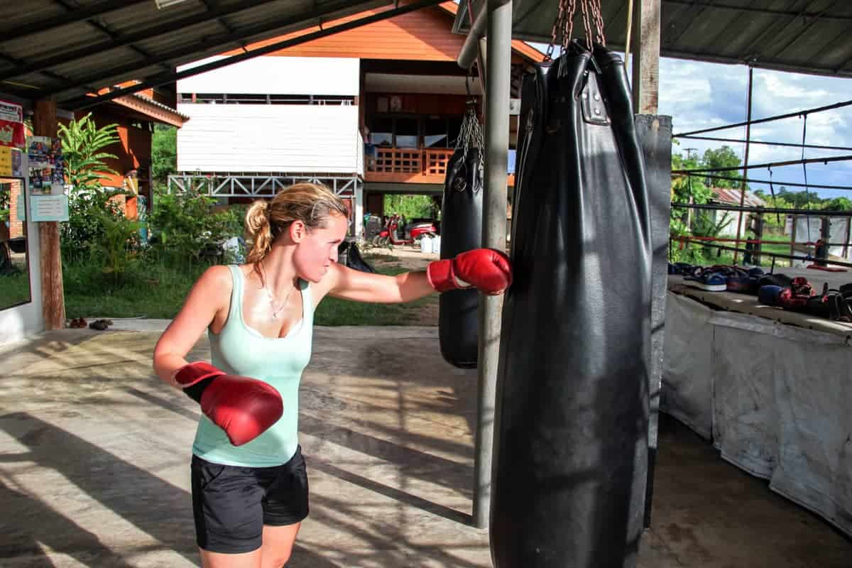 Woman in Muay Thai training in Thailand, practicing on a hanging black punch bag