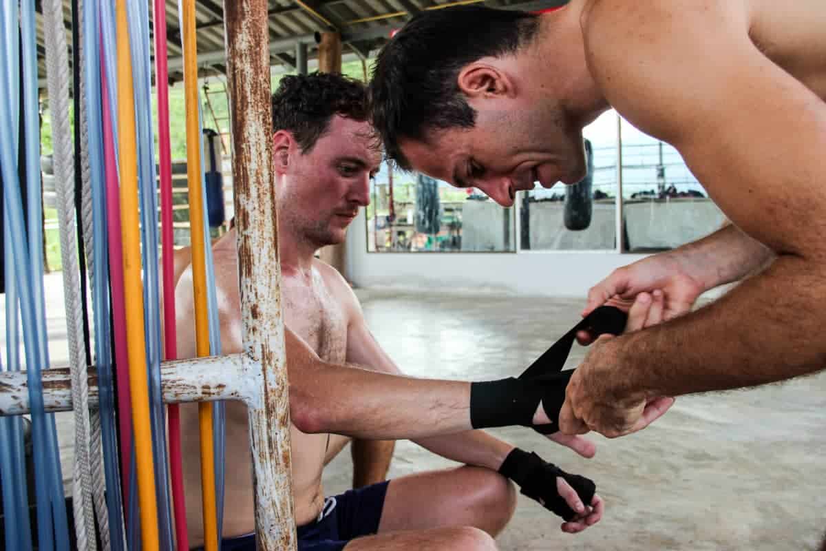 Instructor de Muay Thai ayudando a un hombre a ponerse vendas en la mano antes de entrenar. 