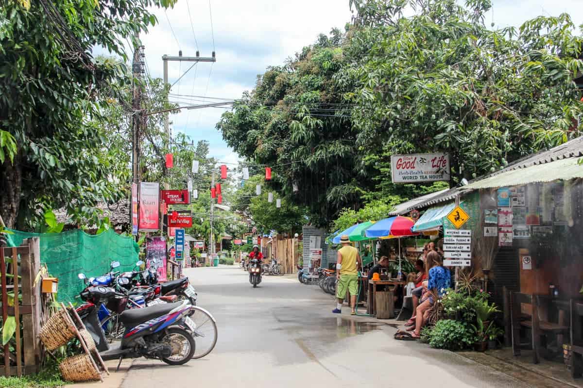 A narrow street lined with big trees and filled with colourful stores in Pai, Thailand