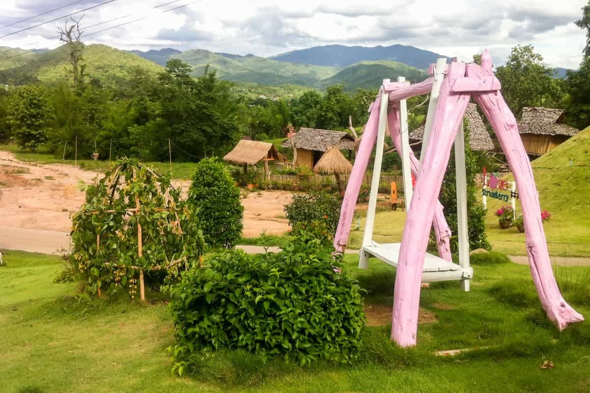 A candy pink wooden swing stands out in the green and yellow hillside in Pai, northern Thailand