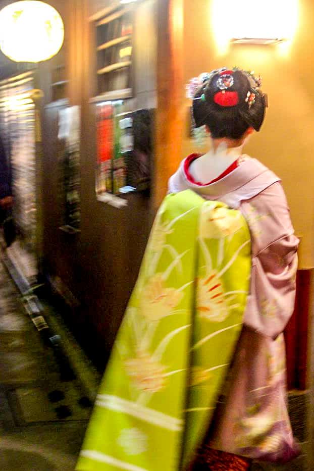 A Geisha in Kyoto, Japan, wearing a pink robe with a green back sash. 