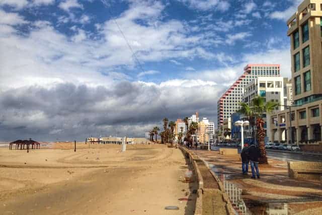 A long stretch of golden sand beach curving to the left. On the right are modern high rise buildings lining the promenade next to the beach.