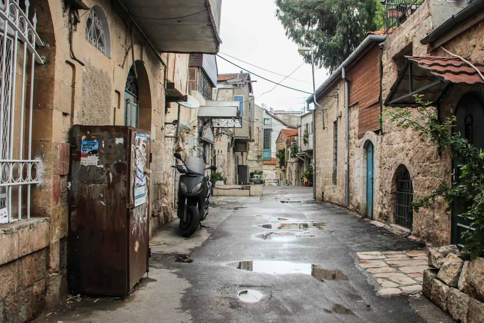 A Jerusalem street of low rise houses built with the local honey stone. A blue door can be seen on the right.