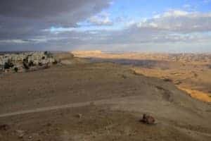 A vast, Mars-like desert landscape of Israel, where a collection of buildings marking a small town can be seen in the lefthand corner.