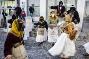 Six people in costumes of white skirts and dark, animal like masks - dancing on the cobblestone streets during a carnival in Skyros island, Greece.