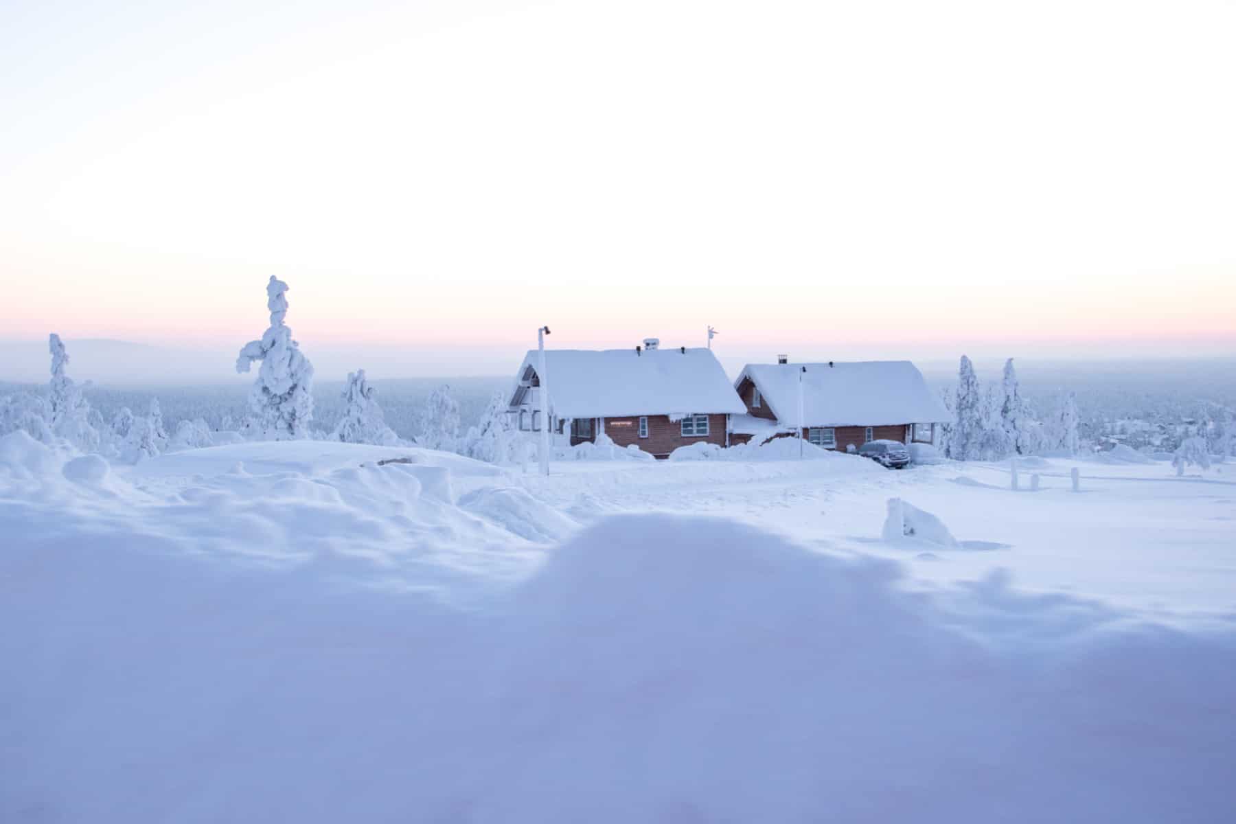 Two gingerbread style houses stand within a pure white snow drenched forest landscape. Apart from trees, there's nothing else in this wilderness of Finnish Lapland. 