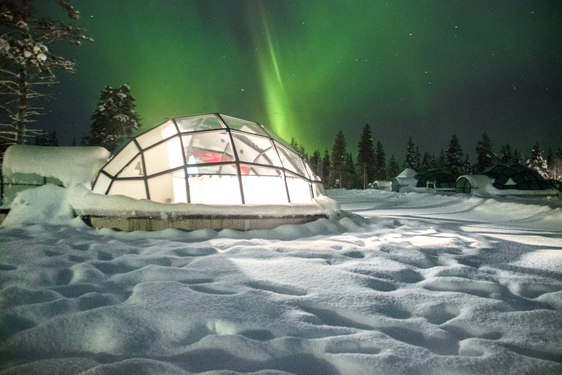 A glass igloo on white snow under the green northern lights in Finland Lapland.