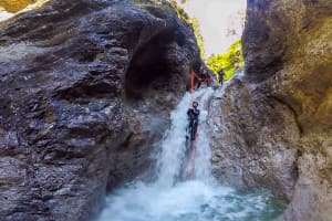 A woman slides down a waterfall in a rocky gorge, canyoning Tirol in Austria