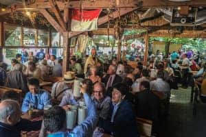 A typical German beer hall filled with a mass of people at long wooden tables and raising large glasses.