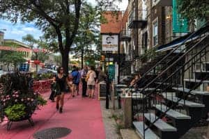 A pedestrian street in Montreal painted in a pinky-red. the buildings on the street are lined with staircases and trees.