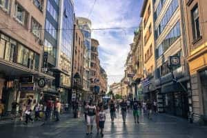 People walking in one of the high streets in the modern part of Belgrade city, flanked by modern concrete and glass-fronted buildings.