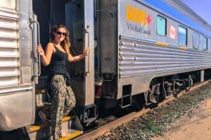 A woman stands in the doorway of a Via Rail train carriage in Canada, while the train is parked on the tracks.