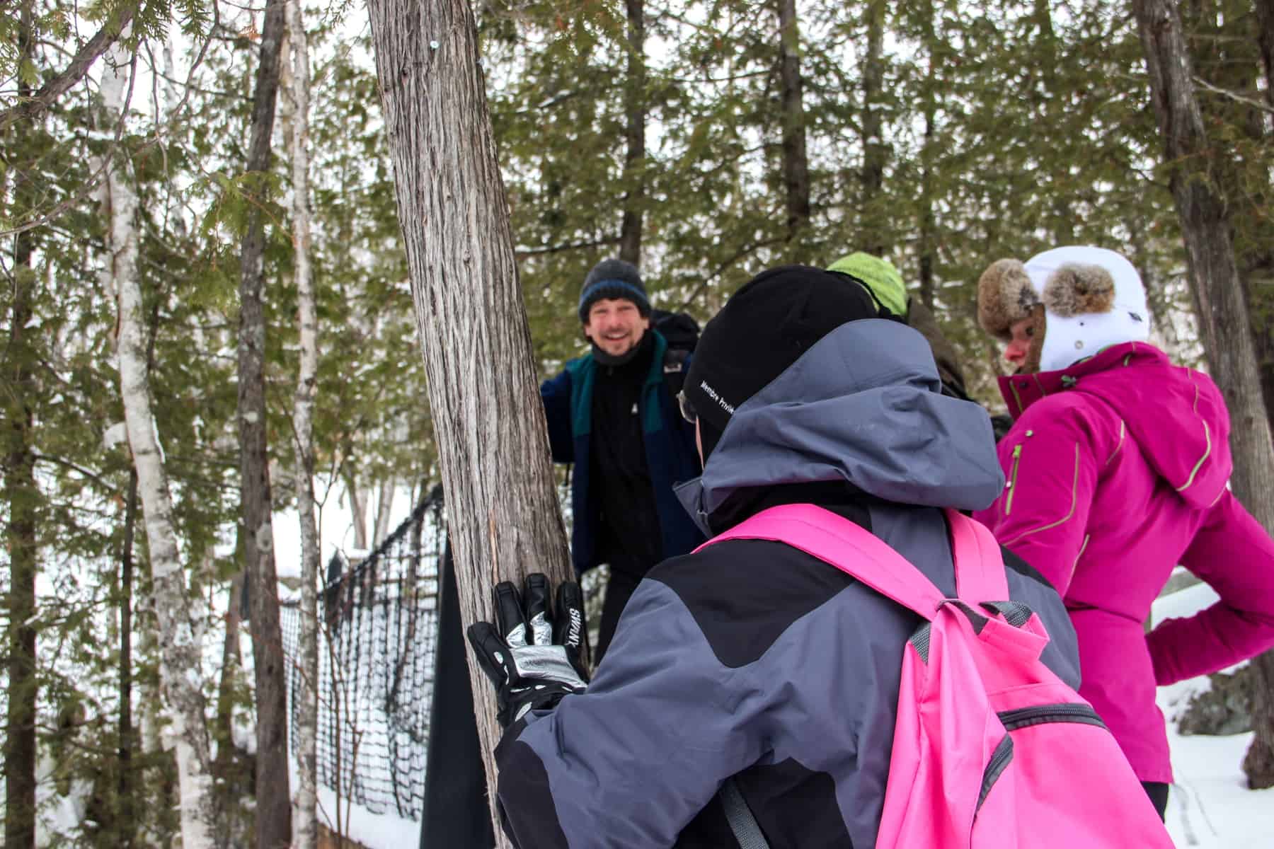 A man in dark clothing leads two people across an elevated bridge in a snow covered forest on a snowshoe tour in Mont Tremblant.