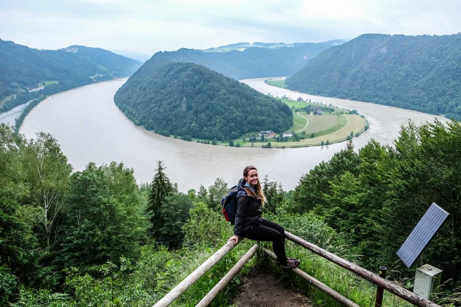 A woman sits at a viewpoint overlooking the Schlögener Schlinge bend in the Danube River, Austria