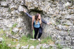 A woman stands within the window archway that's a small part of the silver rocky ruins of an ancient site in Ireland.