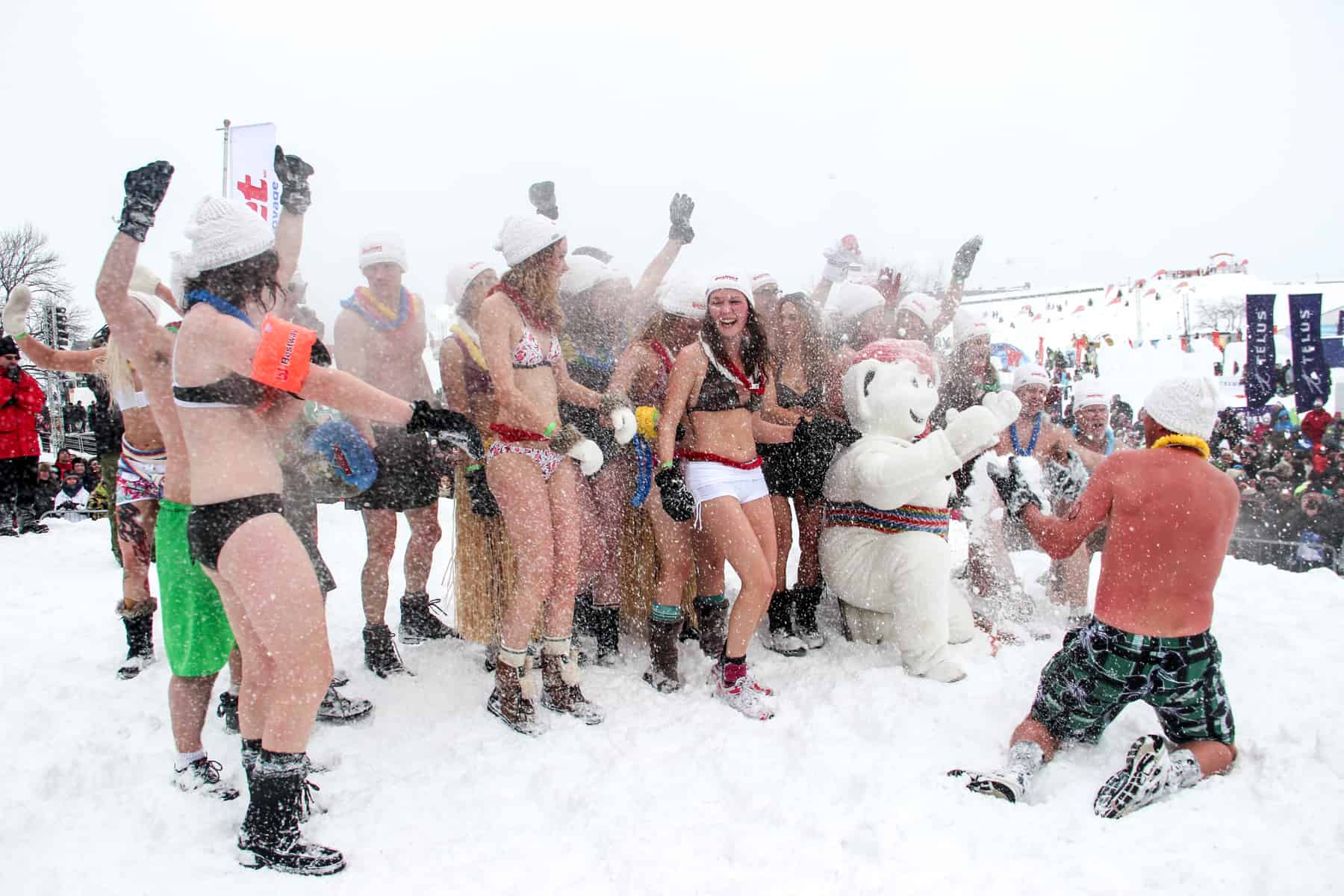 A group of people in swimwear and white hats have a snowfight with the snowman figure, Bonhomme, during the Snow Bath at the The Carnival de Quebec.