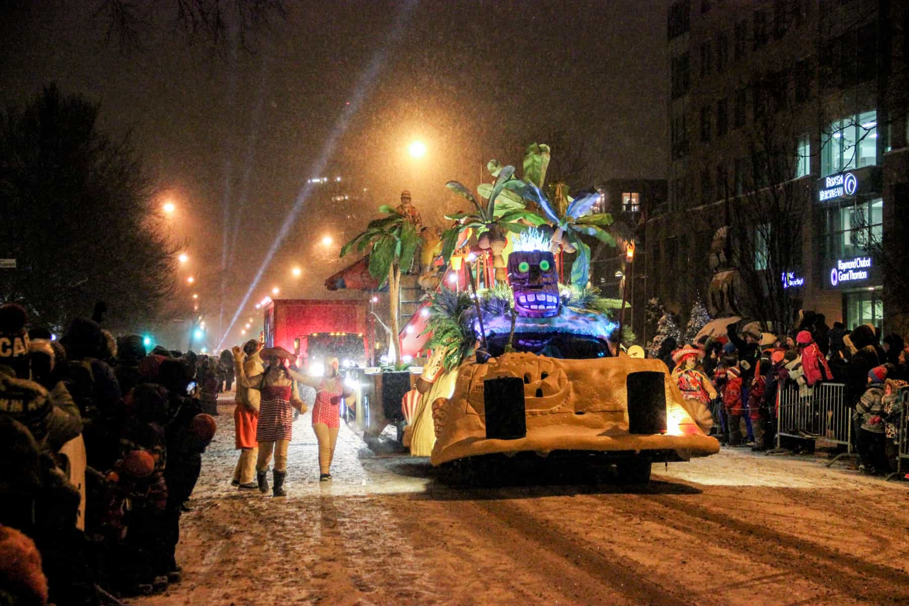 People line either side of the snow covered street watching a carnival parade and jungle themed float, in Quebec city in winter.