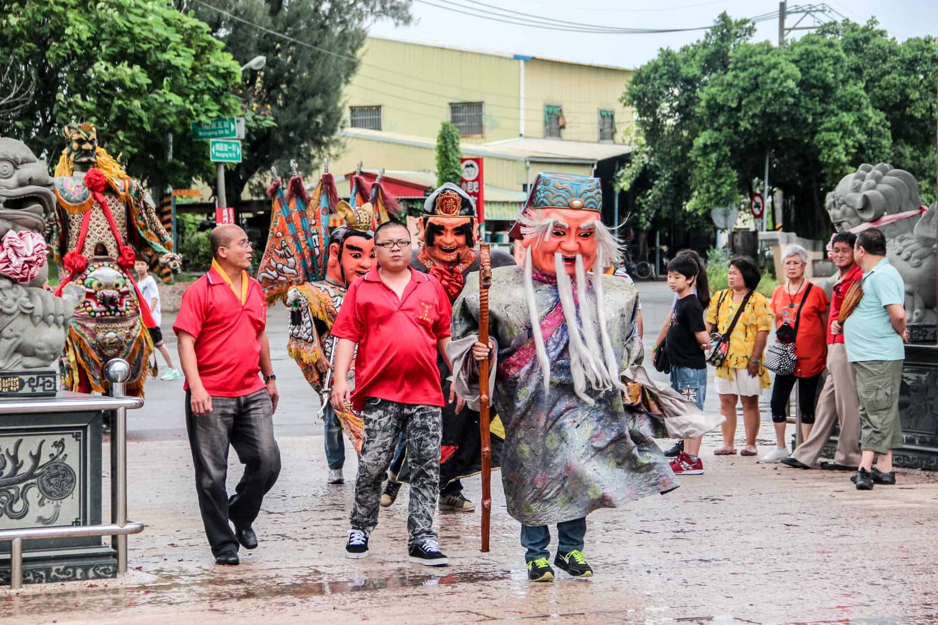 Men in red t-shirts leading people in folk costume at a traditional ceremony at Tainan's Luermen Matsu Temple. 