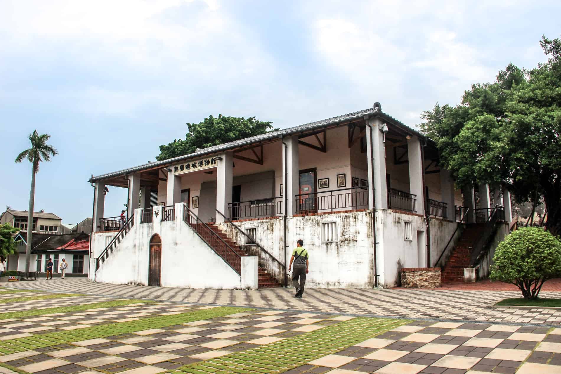 A man walking on a chequered pavement towards the colonial style white building of the Fort Zeelandia Museum in Tainan. 