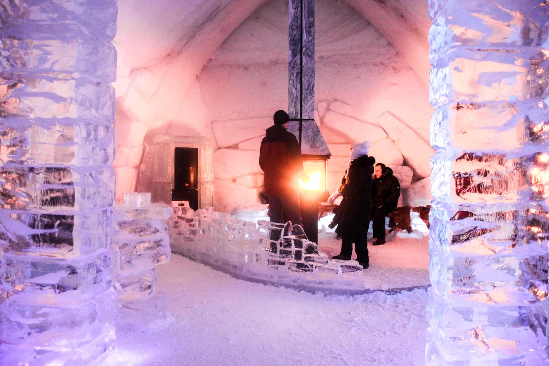 People gathering around a fire in a bar made entirely of ice in Quebec's ice hotel, Hôtel de Glace.
