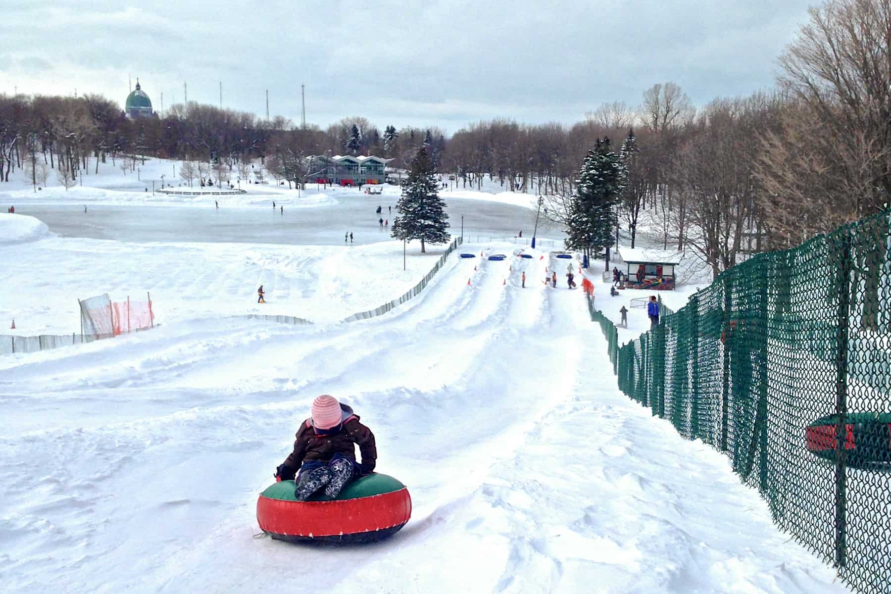 A child on a green and red rubber tube slides down a pathway carved out of snow on Mont Royal, Montreal. 