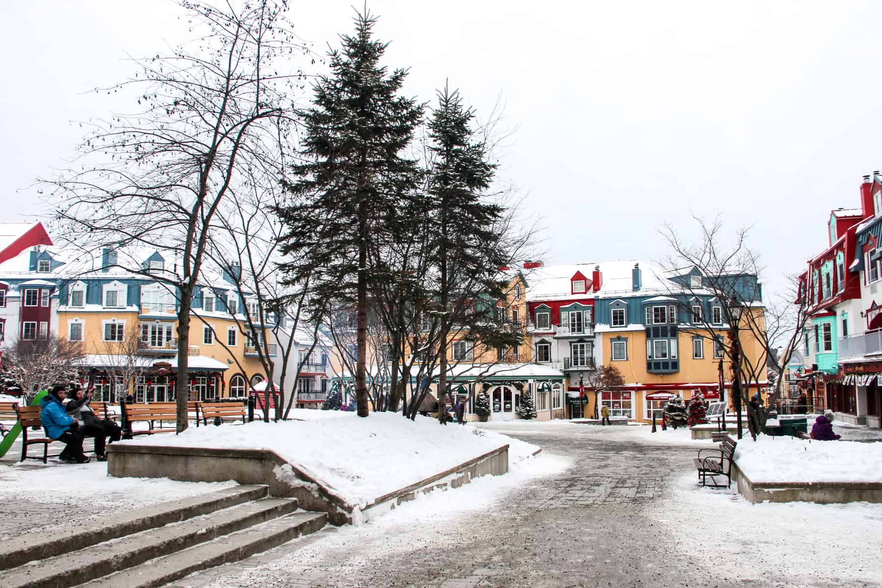 People sitting outside a blue and orange painted corner building in Mont Tremblant's winter village. 