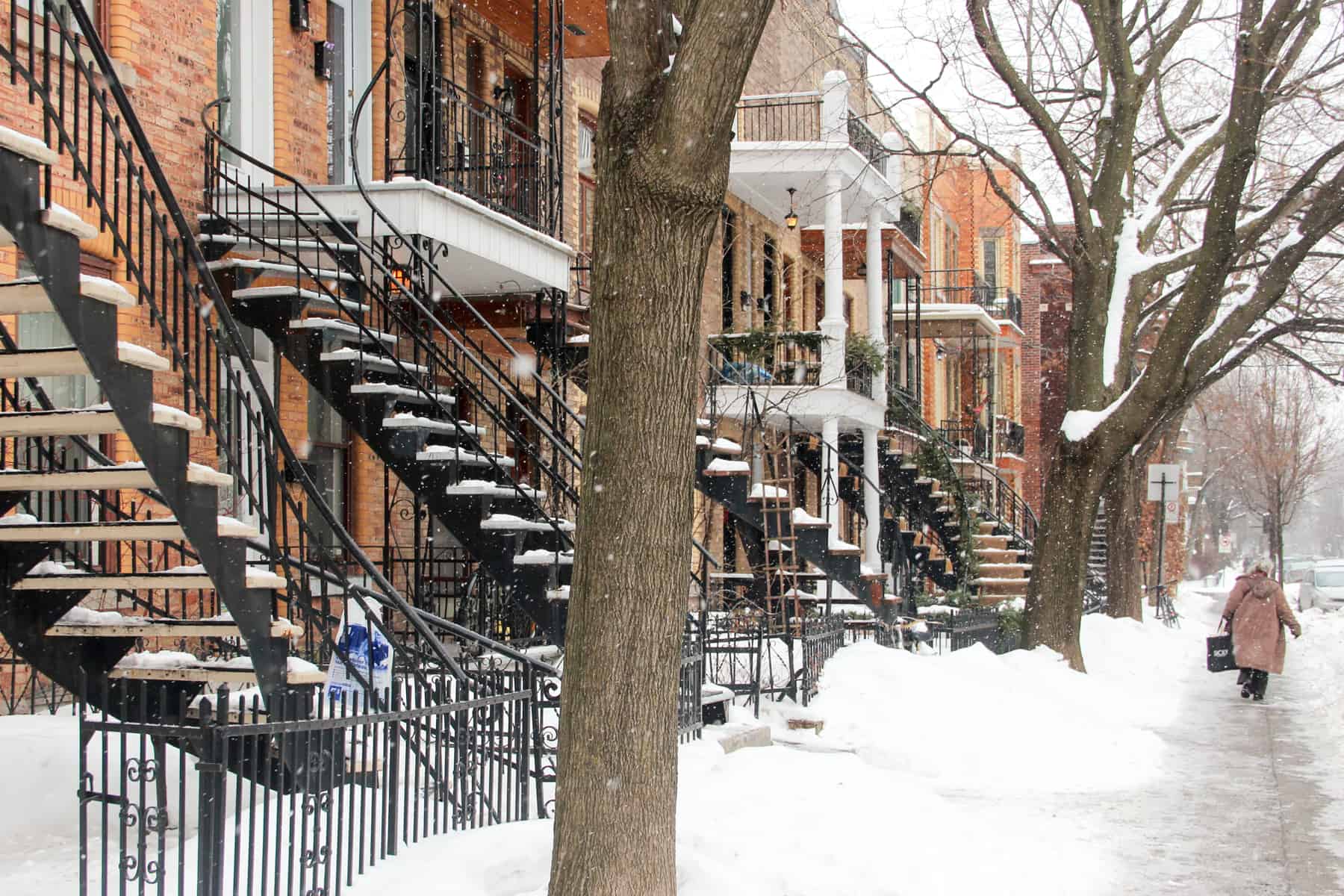  A person walks on pathway covered in snow next to a row of famed Montreal staircases that are an architectural features of houses here. 