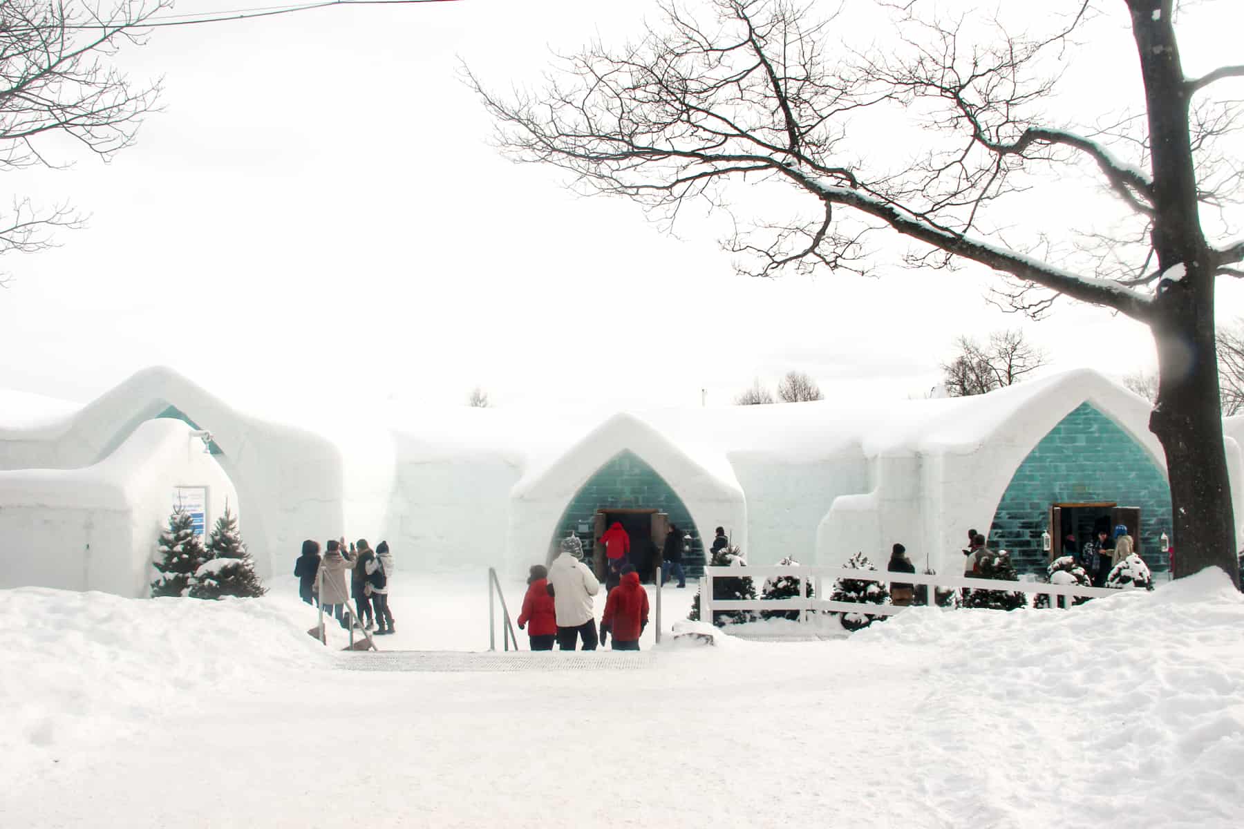 People walking towards the bright white and blue ice exterior of Quebec's ice hotel, Hôtel de Glace.