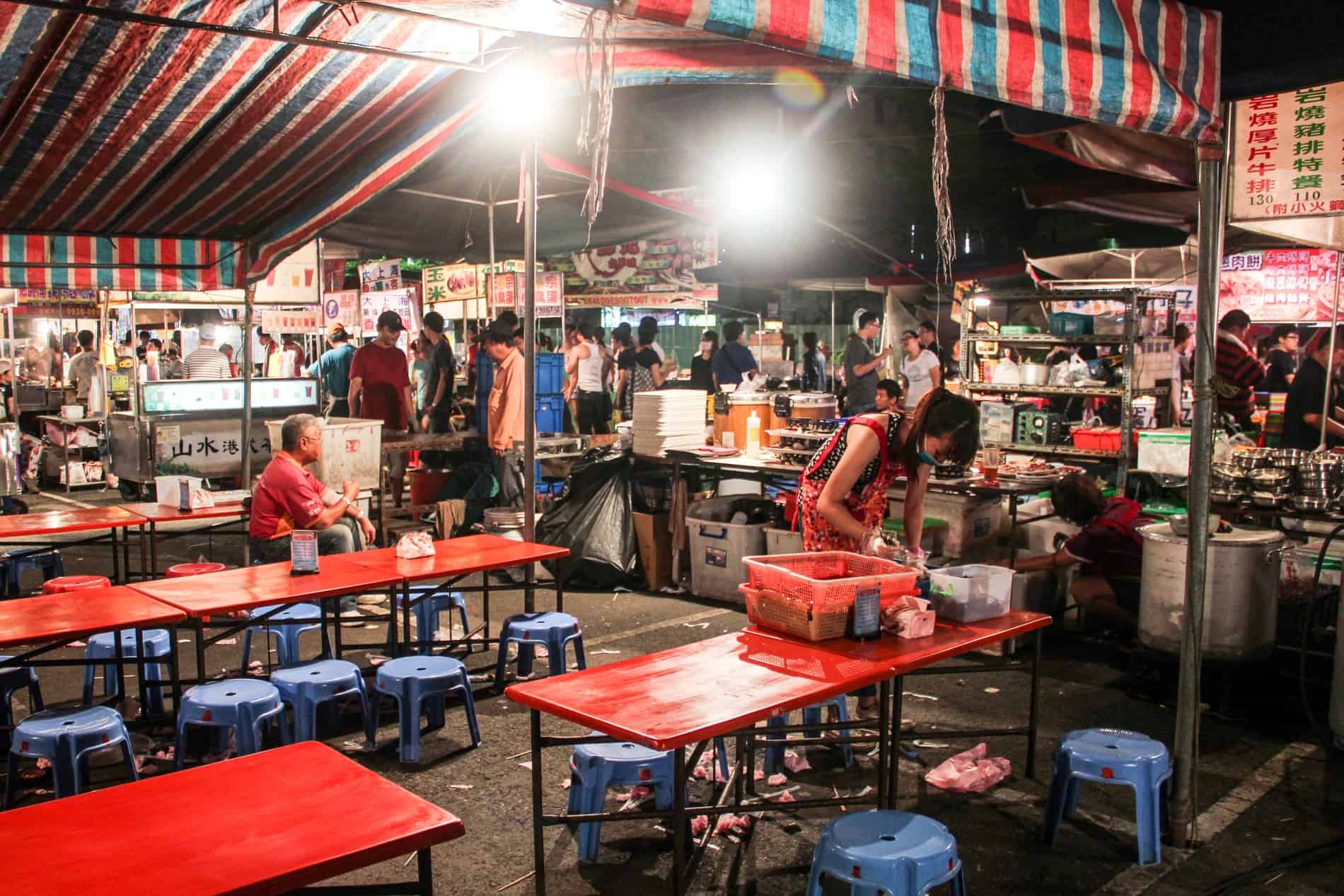 Red tables and blue chairs behind a food vendor at one of Tainan's Night Markets. 