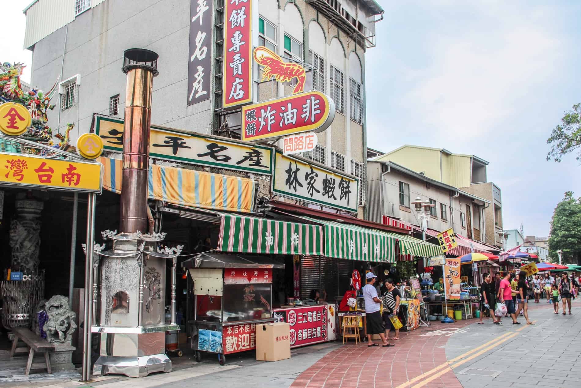 People on a street lined with shops and street food vendors in Tainan city centre. 