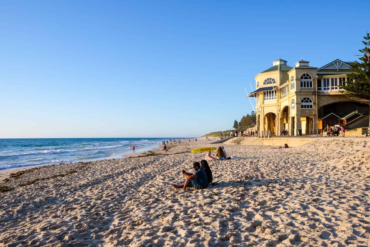 The thick white sands of Cottesloe Beach in Perth with the yellow pavilion hall behind