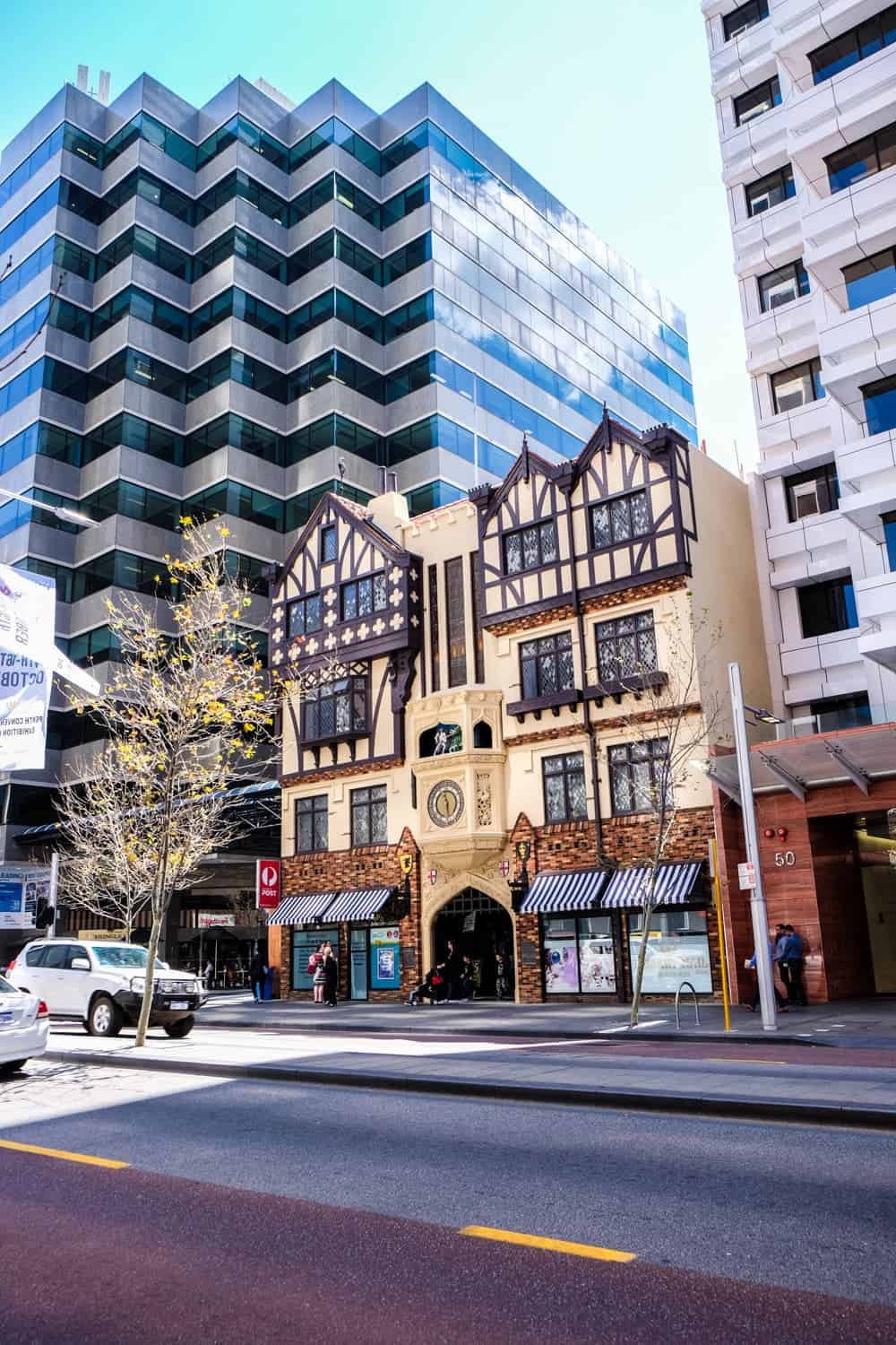 A small, stately designed building sits wedged in between two tall modern structures in Perth, Australia