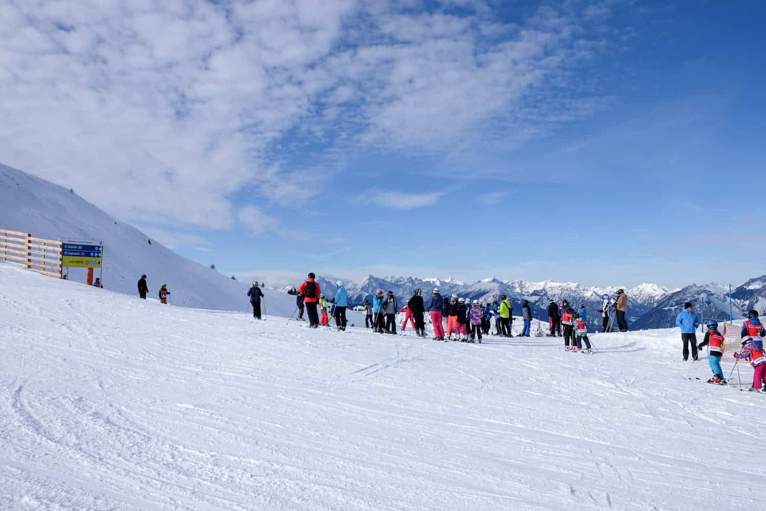 A group of skiers in colourful clothing at the top of a snowy mountain.