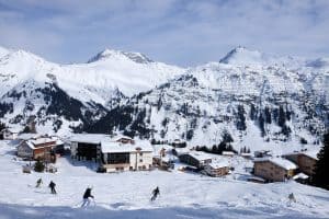 People skiing on a slope in front of mountain huts backed by the Alps mountains in Lech, Austria.