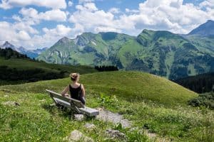 A woman sits on a bench overlooking the rolling green mountain hills during summer in Lech, Austria.
