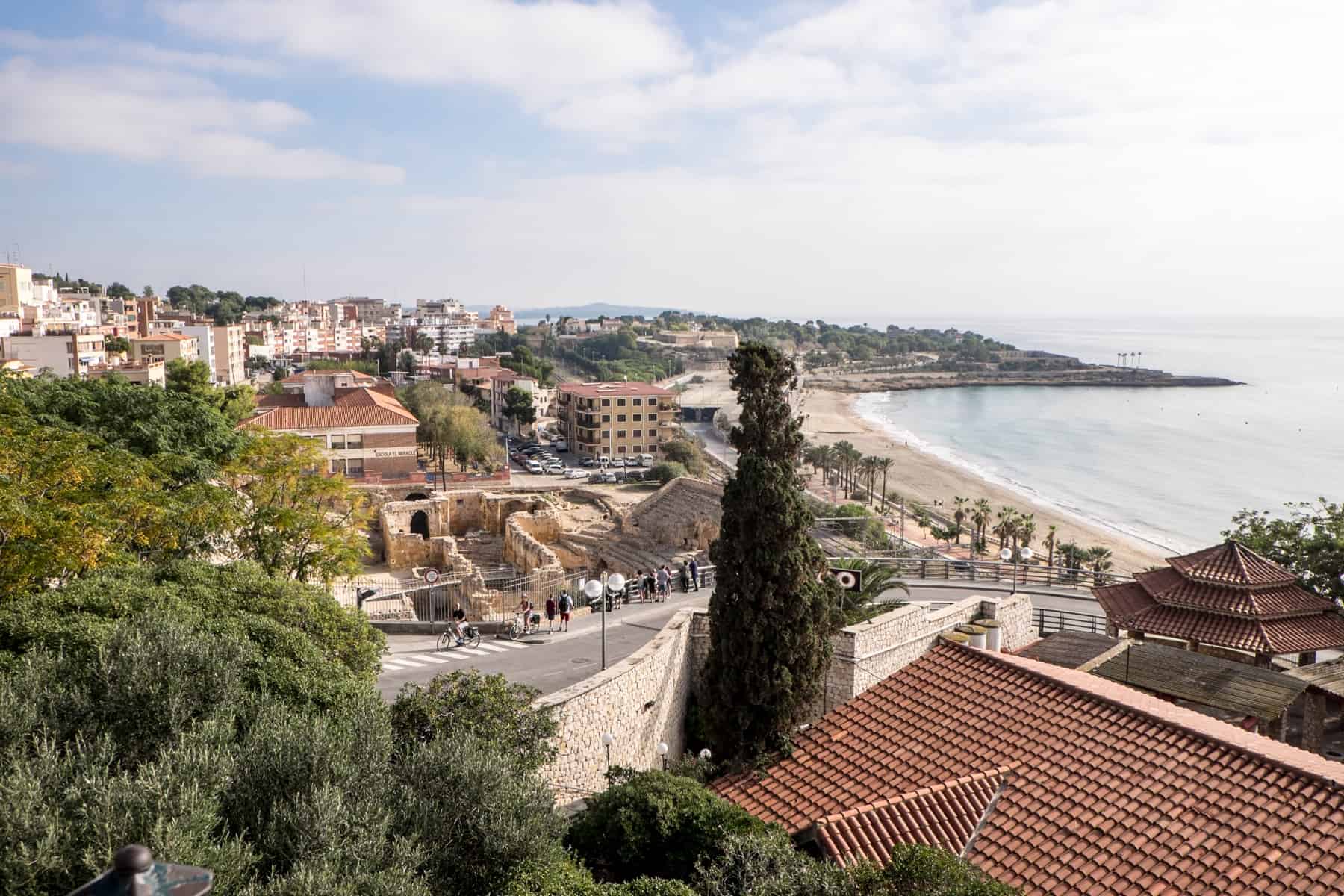 Roman ruins and the sandy yellow and orange hued low rise buildings line the coast, making up the city of Tarragona, Spain.