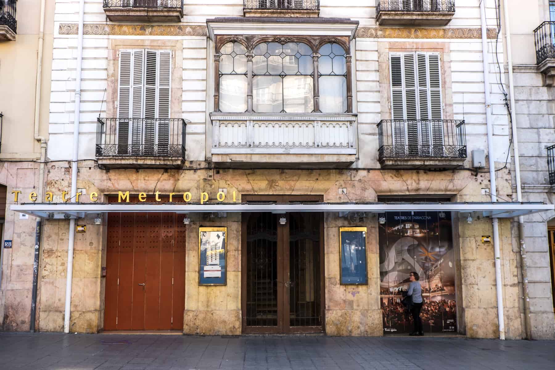 A woman walks past the golden stone (lower part) and white clad (upper part) building of the Theatre Metropole in Tarragona, Spain