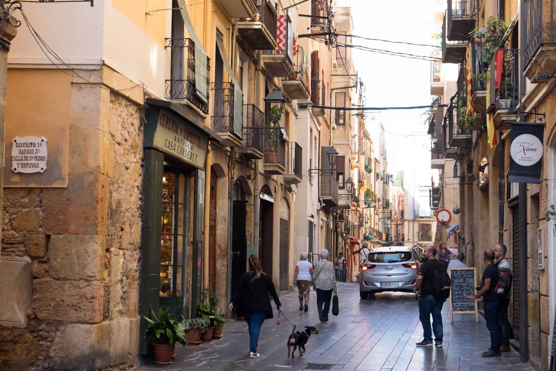 A woman walks with her dog and people gather in the golden yellow streets of Tarragona, Spain. 