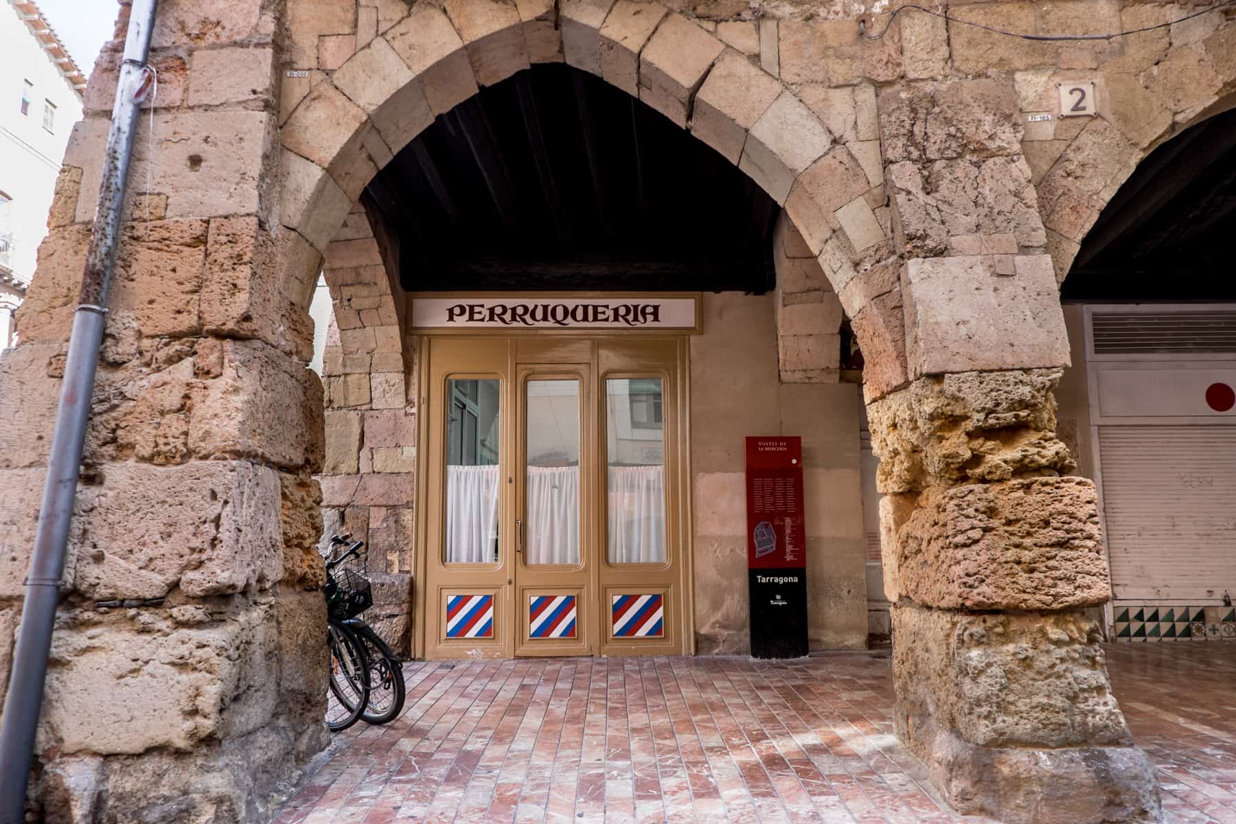 A shop entrance with caramel coloured doors within a roman stone archway in Tarragona, Spain