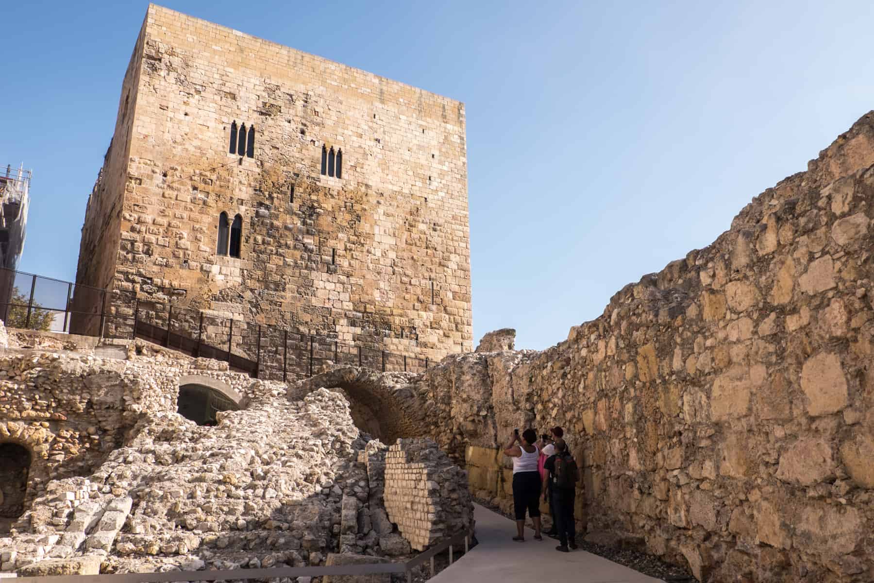 Three people inside the Roman Circus in Tarragona, taking pictures of the square tower structure