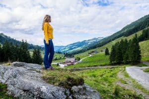 A woman stands on a grey rock looking out across the rolling green Wildschönau Valley in Tirol, Austria