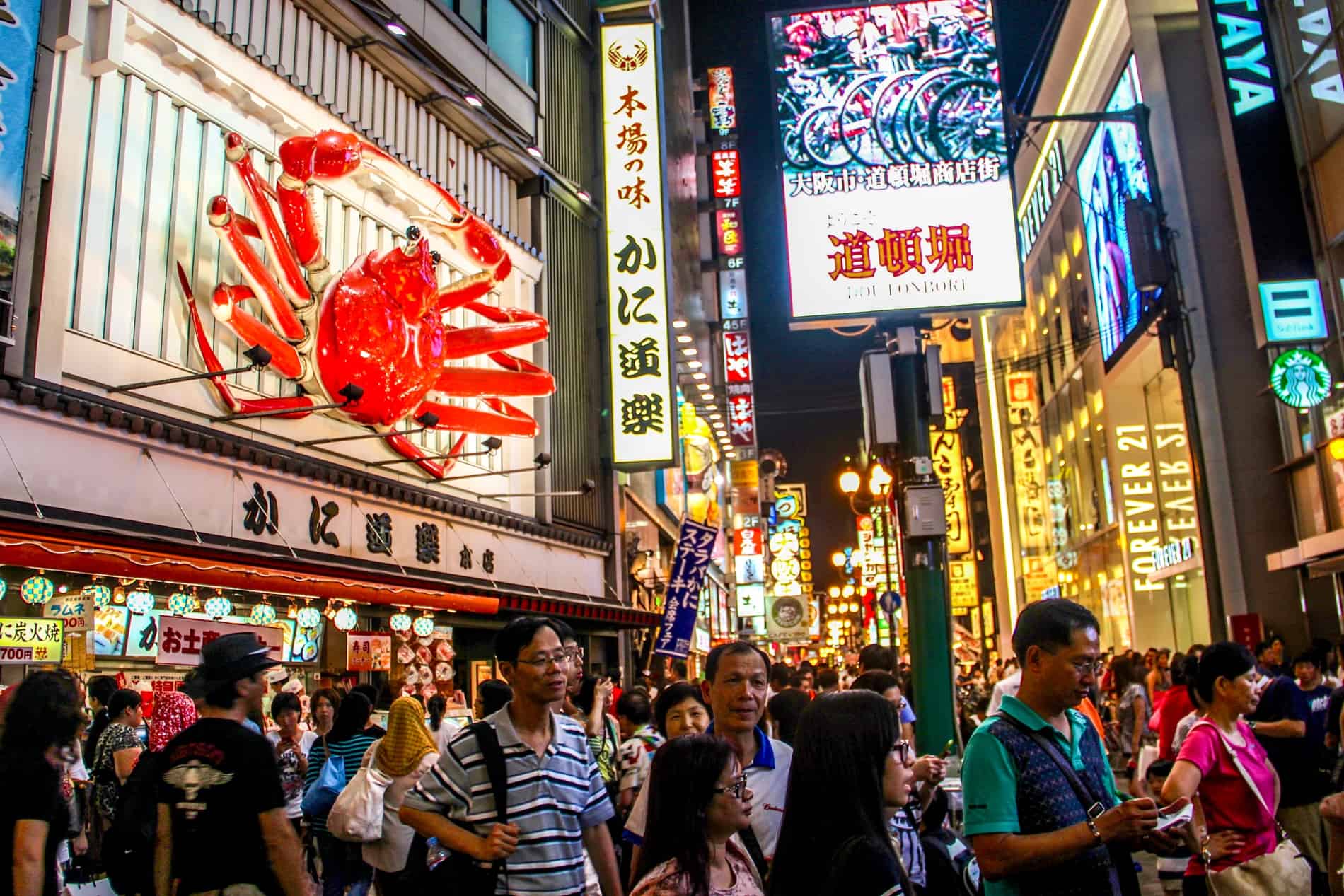 The busy Dotonburi area of Osaka at night. The street is crowded with people walking past a shop front to the left with a giant red crab above it. 