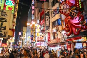 Dotonburi Street in Osaka at night, full of people and with buildings covered with lit-up signage, posters, and giant pink octopus.