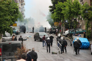 Riot police on a hilly street in Istanbul dispersing protesters. Smoke can be seen in the background.